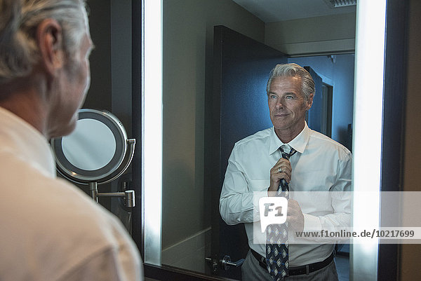 Caucasian businessman adjusting tie in mirror