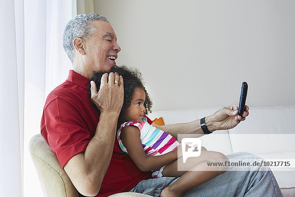 Grandfather and granddaughter taking selfie in living room
