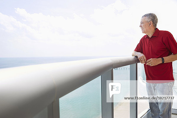 Older Black man overlooking ocean from balcony