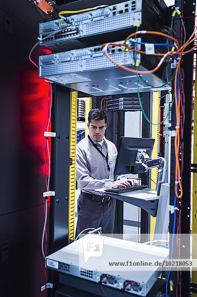 Hispanic technician using computer in server room