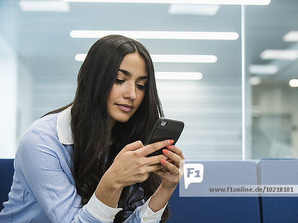 Mixed race businesswoman using cell phone in office lobby