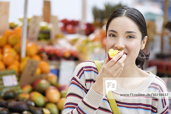 Hispanic woman eating fruit at farmers market