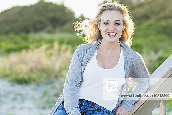 Smiling Caucasian woman sitting on banister over beach