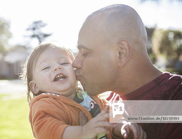 Close up of Hispanic father kissing cheek of son outdoors