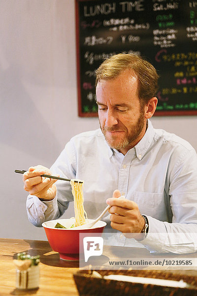 Caucasian man with beard eating ramen noodles