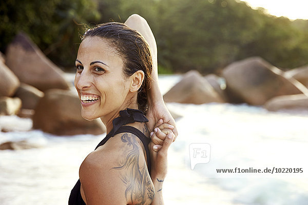 Seychelles  portrait of smiling woman with tatoo doing yoga exercise on the beach