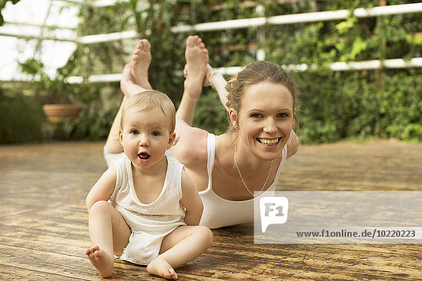 Porträt eines Babys  das vor der Mutter sitzt und Yoga-Übungen macht