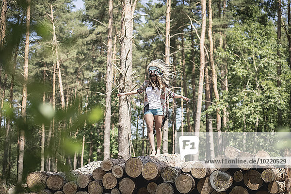 Junge Frau verkleidet sich als Indianerin  die auf einem Holzstapel balanciert.