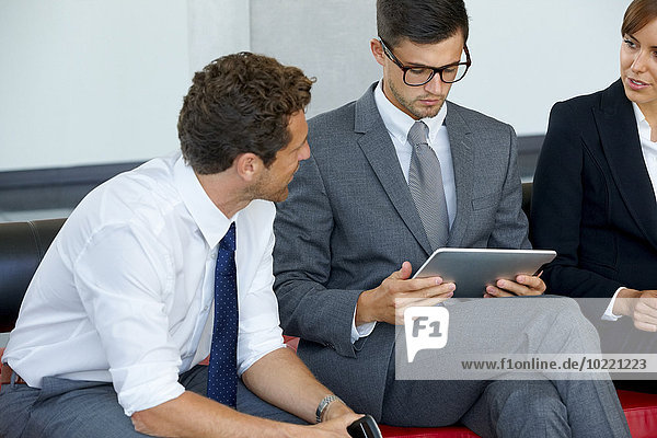 Drei Geschäftskollegen mit digitalem Tablett diskutieren in der Büro-Lobby