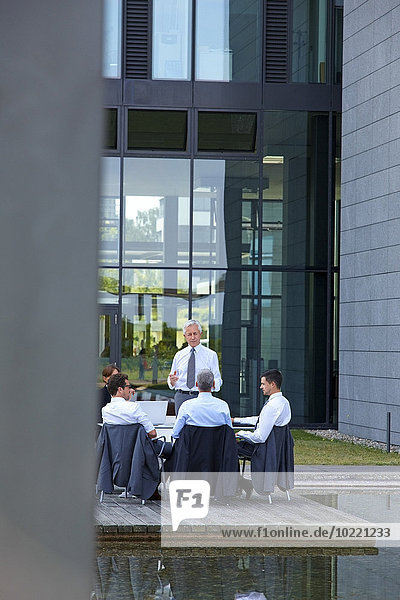 Manager im Gespräch mit Mitarbeitern auf Stühlen vor dem Bürogebäude