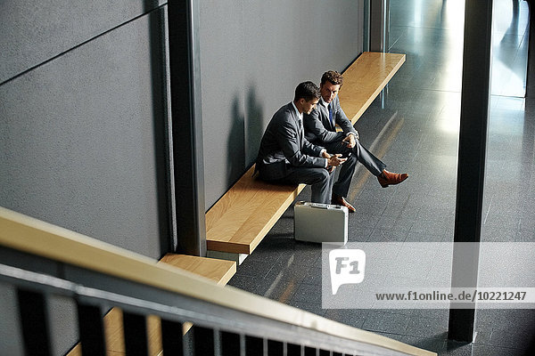 Zwei junge Geschäftsleute sitzen auf der Bank und telefonieren in der Bürolobby.