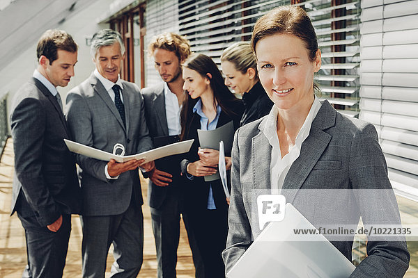 Mature businesswoman with colleagues looking at a business file in background