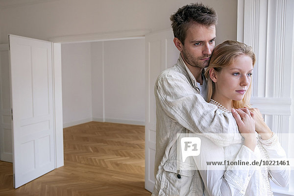 Junges Paar in leerer Wohnung schaut in Gedanken weg