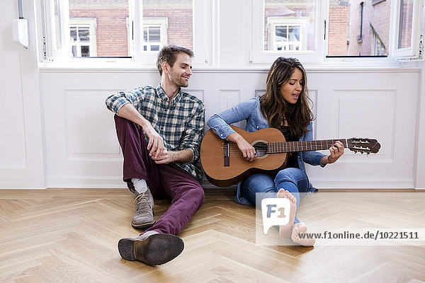 Young couple sitting on floor with woman playing guitar