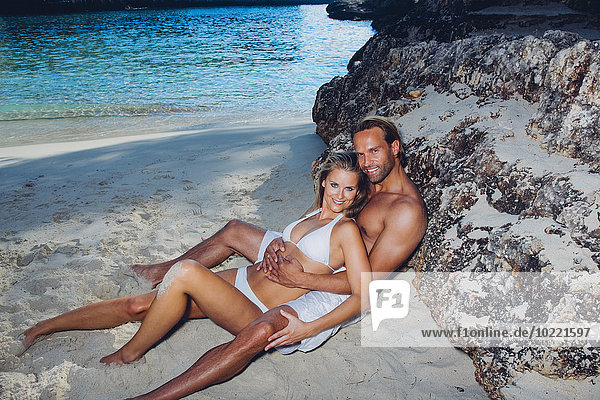 Spanien  Mallorca  lächelndes Paar  das sich gegen einen Felsen am Strand lehnt