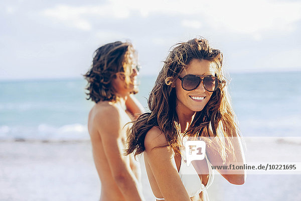 USA  Miami  portrait of young woman in bikini on the beach with her boyfriend in the background