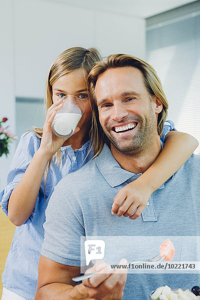 Porträt eines glücklichen Vaters und einer glücklichen Tochter  die Milch trinken und Salat essen.