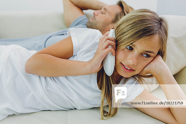 Mädchen auf der Couch liegend  Telefon mit Vater im Hintergrund
