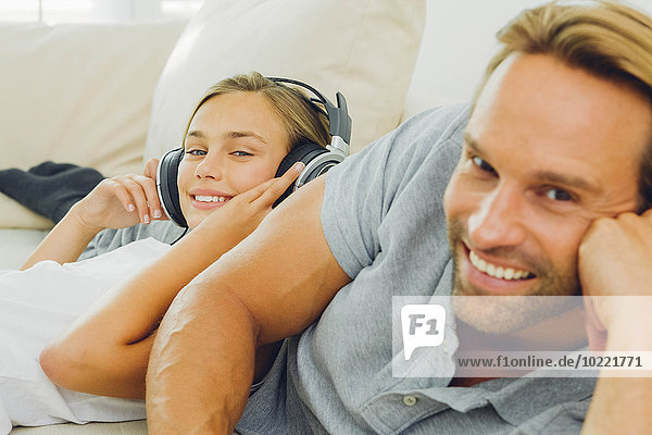 Mädchen auf der Couch liegend mit Vater beim Musikhören
