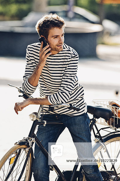 Junger Mann mit Fahrrad telefoniert mit seinem Smartphone