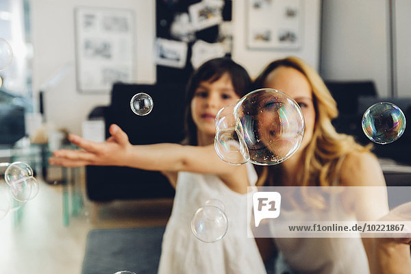 Happy mother with daughter at home blowing soap bubbles