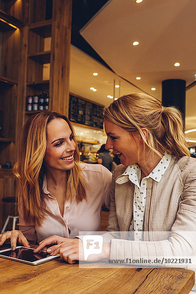 Two female friends with digital tablet communicating in a coffee shop