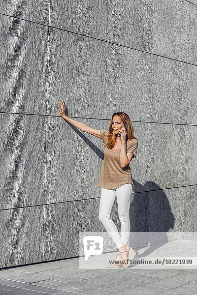 Young woman leaning on a wall talking on mobile phone