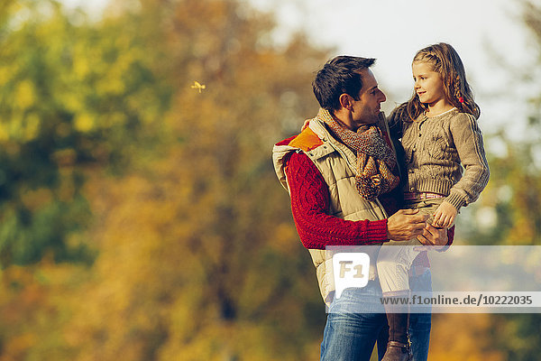 Vater trägt seine kleine Tochter an einem Herbsttag im Park.