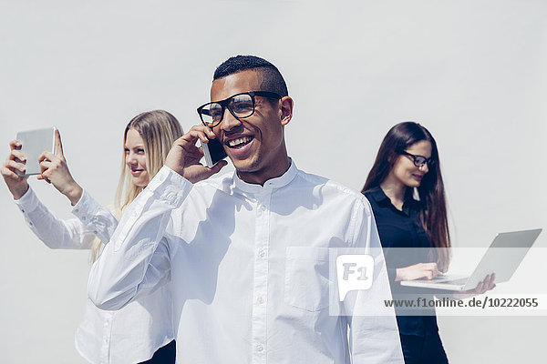 Three stylish young people with mini tablet  smartphone and laptop in front of white background