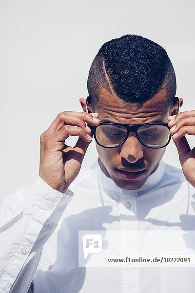 Portrait of young man with shaved hair and glasses wearing white shirt in front of white background