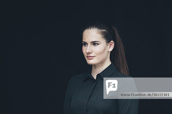 Portrait of young woman with ponytail in front of black background