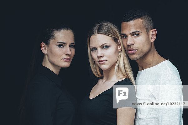 Group picture of two young woman and young man in front of black background