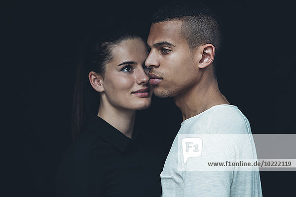 Porträt des jungen Paares Kopf an Kopf vor schwarzem Hintergrund