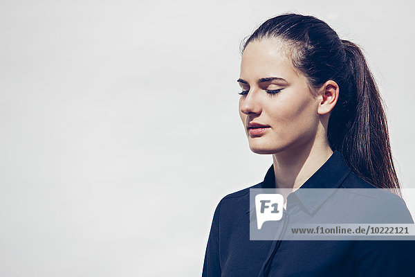 Portrait of young woman with ponytail and closed eyes in front of white background