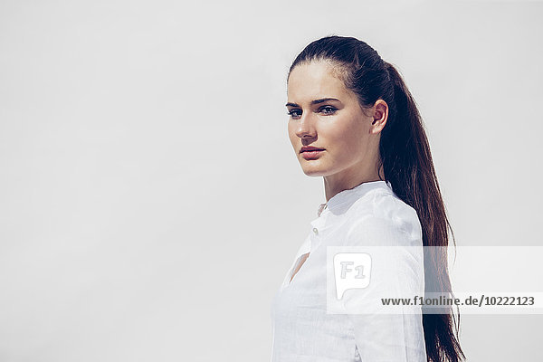 Portrait of young woman with ponytail wearing white blouse in front of white background