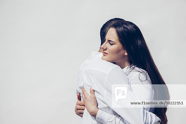White dressed lovers with dark hair caressing each other in front of white background