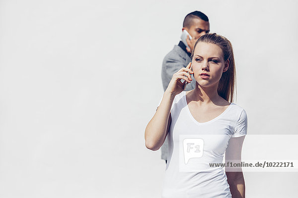 Porträt einer jungen Frau beim Telefonieren mit Smartphone vor weißem Hintergrund