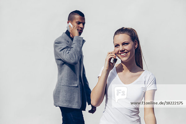 Porträt einer lächelnden jungen Frau beim Telefonieren mit dem Smartphone vor dem jungen Mann