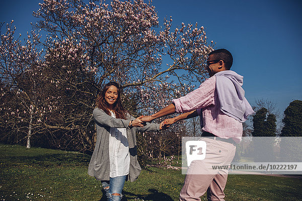 Glückliches junges Paar hält sich im Park an den Händen.