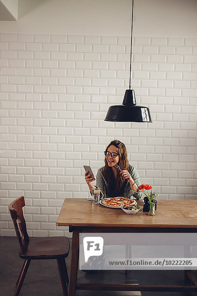 Junge Frau beim Pizzaessen im Restaurant  mit dem Handy