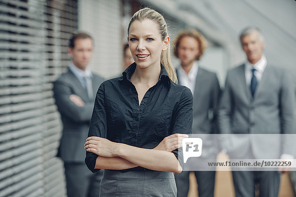 Young businesswoman standing with arms crossed  colleagues in background