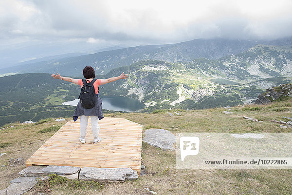 Bulgarien  Rila-Gebirge  Rückansicht der älteren Frau mit ausgestreckten Armen mit Blick auf die Ansicht