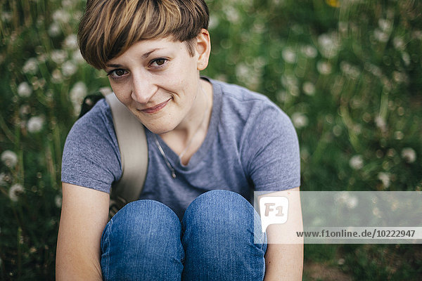 Porträt einer lächelnden jungen Frau auf einer Wiese sitzend