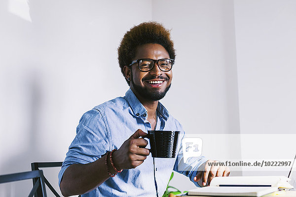 Smiling young man at home office having a coffee break
