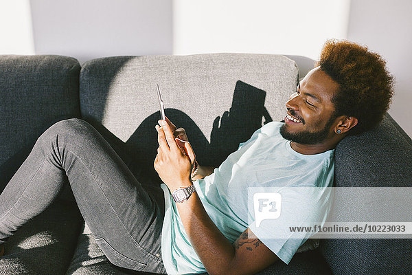 Young man at home reading messages on smart phone