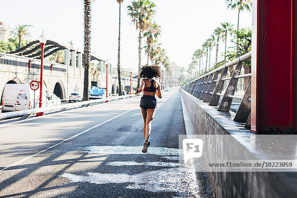 Spanien  Barcelona  Rückansicht der joggenden jungen Frau auf einer Straße