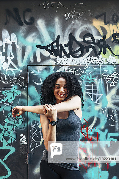 Porträt einer lächelnden jungen Frau vor der Graffiti-Wand