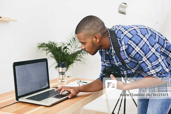 Junger Mann arbeitet mit Laptop in seinem Fotostudio
