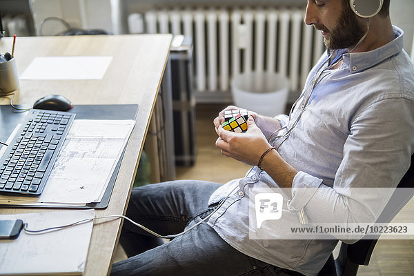 Junger Mann im Büro am Schreibtisch mit Rubik's Würfel