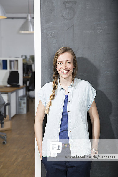Smiling young woman standing at blackboard in office